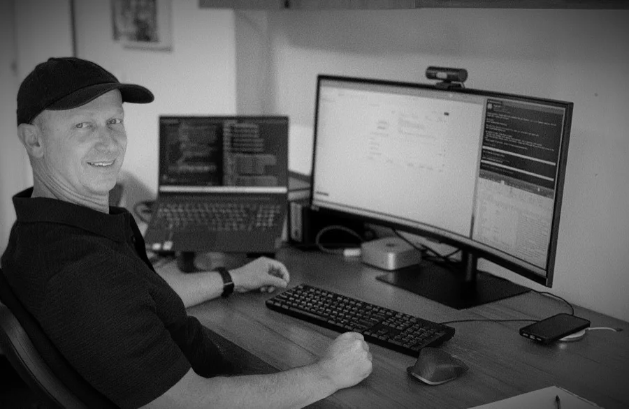 Tim at his desk in Wellington working at a curved monitor and laptop.